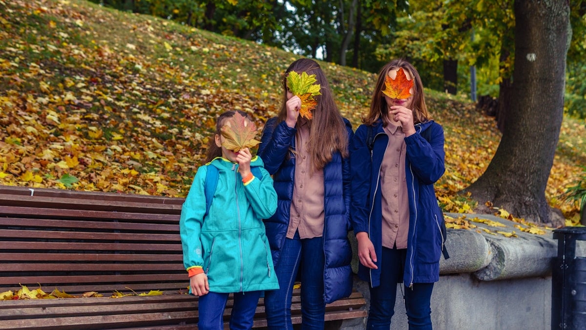 three girls covered their face with colorful autumn leaves in the autumn park
